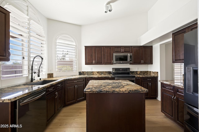 kitchen featuring light wood-type flooring, a sink, a center island, dark brown cabinetry, and appliances with stainless steel finishes