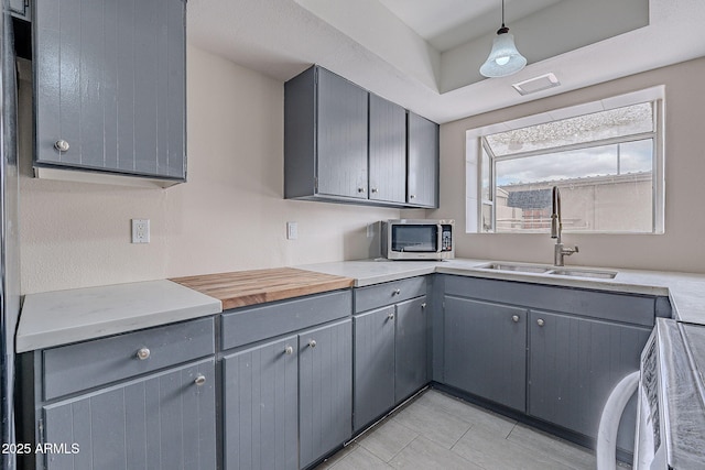 kitchen featuring a sink, stainless steel microwave, gray cabinetry, and light countertops