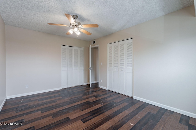 unfurnished bedroom with visible vents, baseboards, dark wood-style flooring, a textured ceiling, and two closets