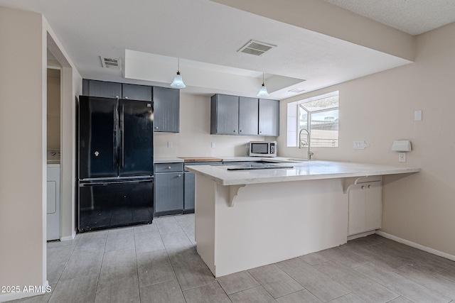 kitchen with visible vents, a sink, stainless steel microwave, freestanding refrigerator, and a peninsula