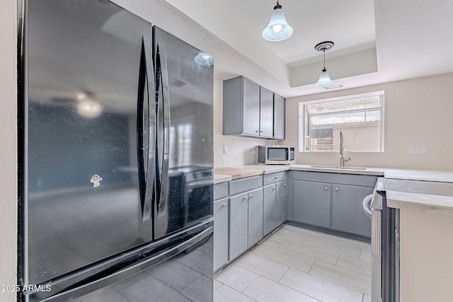 kitchen featuring gray cabinetry, a sink, stainless steel microwave, freestanding refrigerator, and a raised ceiling