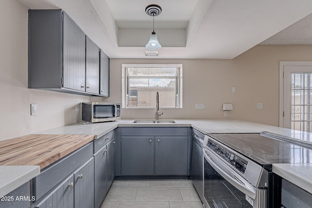 kitchen with light tile patterned floors, a tray ceiling, gray cabinets, a sink, and stainless steel appliances