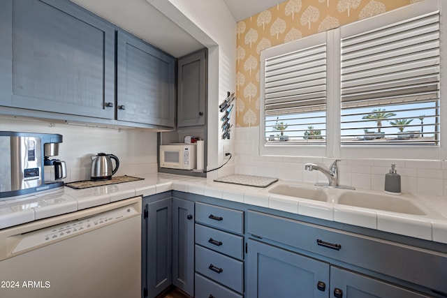 kitchen featuring blue cabinetry, tile counters, white appliances, tasteful backsplash, and sink