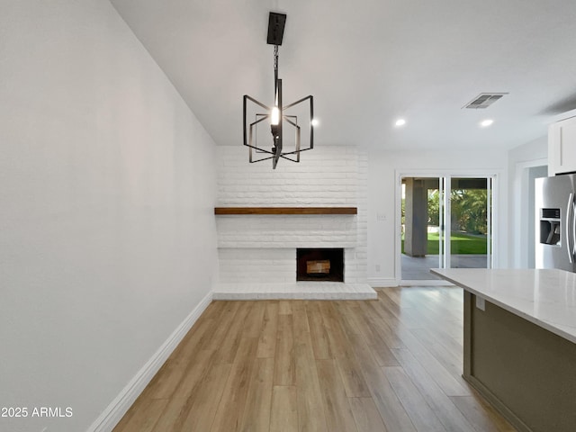 unfurnished living room with visible vents, baseboards, light wood-style floors, a brick fireplace, and a chandelier