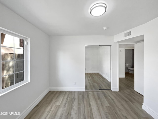 unfurnished bedroom featuring visible vents, baseboards, a closet, and wood finished floors