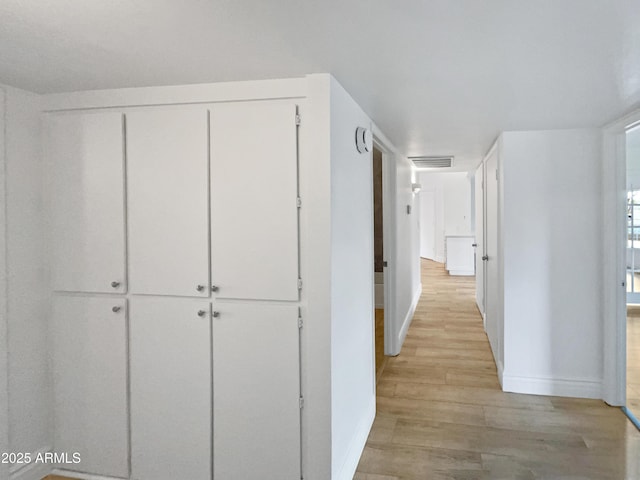 hall with light wood-style flooring, baseboards, and visible vents