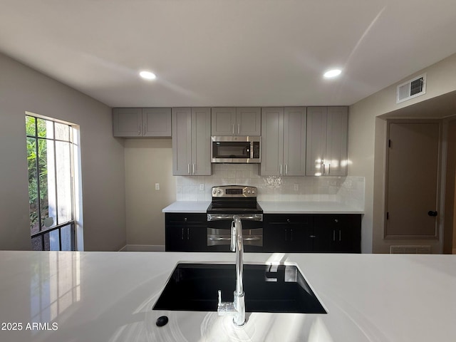 kitchen featuring light countertops, stainless steel appliances, gray cabinetry, and visible vents