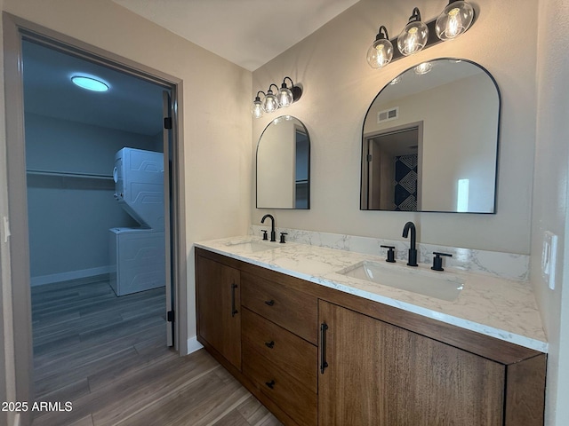 bathroom featuring visible vents, a sink, stacked washing maching and dryer, and wood finished floors