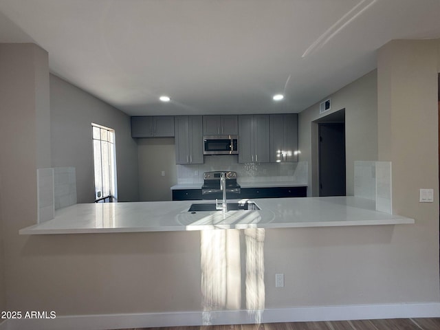 kitchen featuring a sink, tasteful backsplash, stainless steel appliances, and a peninsula