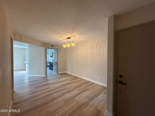 spare room featuring light wood-style floors, baseboards, and a notable chandelier