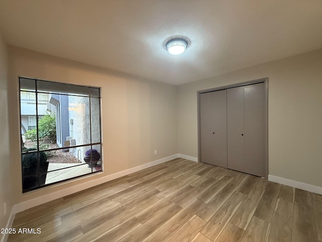 unfurnished bedroom with baseboards, light wood-style flooring, and a closet