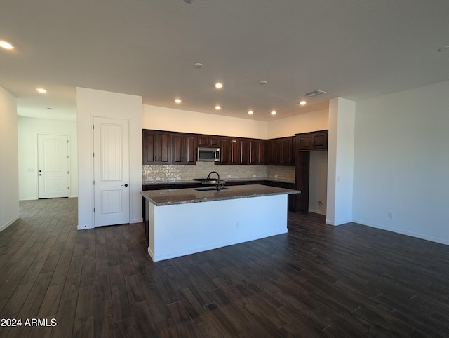 kitchen with dark brown cabinetry, a center island with sink, sink, tasteful backsplash, and dark hardwood / wood-style floors