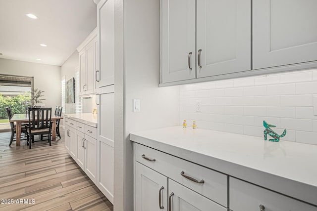 kitchen with decorative backsplash, light countertops, light wood finished floors, recessed lighting, and white cabinetry
