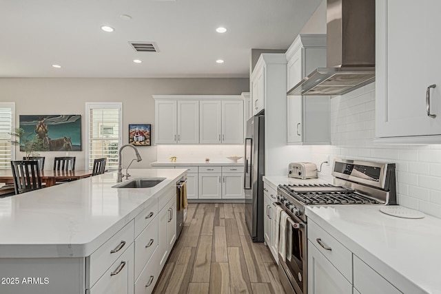 kitchen featuring wall chimney range hood, a sink, stainless steel appliances, recessed lighting, and white cabinetry