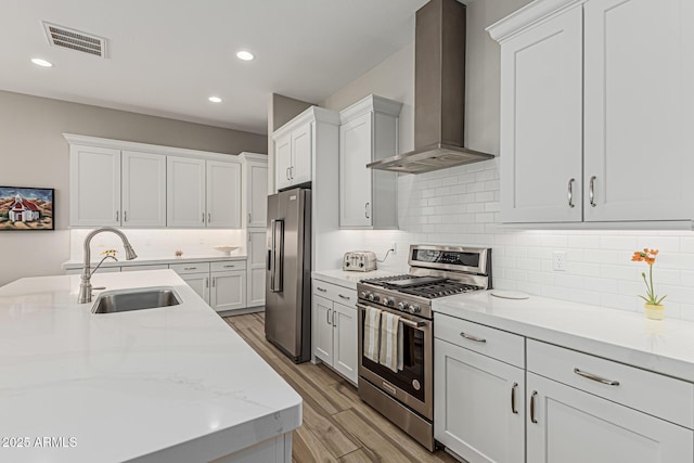 kitchen with visible vents, light wood-type flooring, wall chimney exhaust hood, a sink, and appliances with stainless steel finishes
