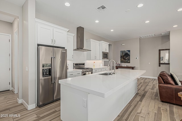 kitchen featuring wall chimney range hood, a kitchen island with sink, visible vents, appliances with stainless steel finishes, and a sink