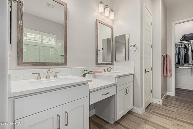 bathroom with a sink, a walk in closet, double vanity, and wood finished floors