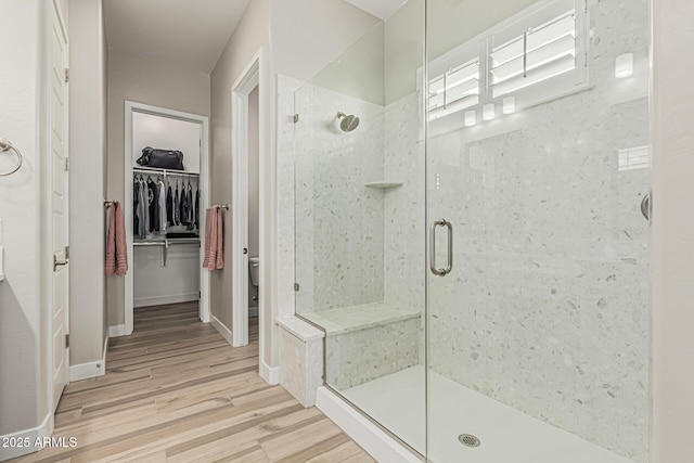 bathroom with a walk in closet, toilet, baseboards, a shower stall, and wood finished floors