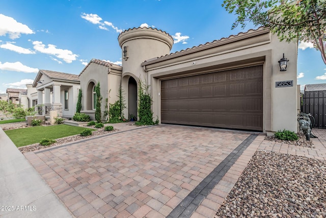 mediterranean / spanish-style home featuring a garage, decorative driveway, stucco siding, and a tiled roof