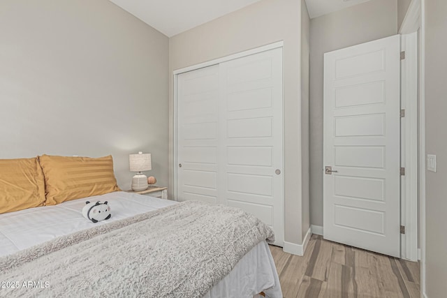 bedroom featuring light wood-style floors, baseboards, and a closet