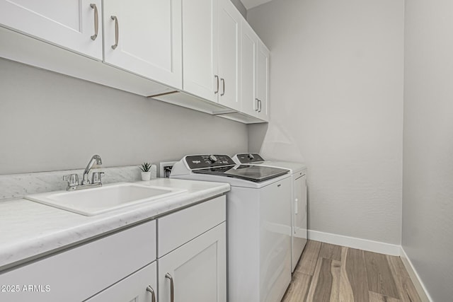 laundry area featuring cabinet space, washer and dryer, a sink, light wood finished floors, and baseboards