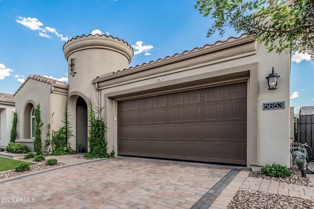 mediterranean / spanish home featuring a garage, decorative driveway, stucco siding, and a tiled roof
