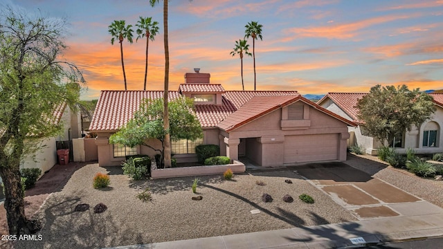 mediterranean / spanish-style home featuring stucco siding, a chimney, an attached garage, and a tiled roof