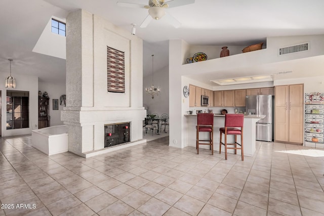 living room with light tile patterned floors, visible vents, high vaulted ceiling, ceiling fan with notable chandelier, and a large fireplace