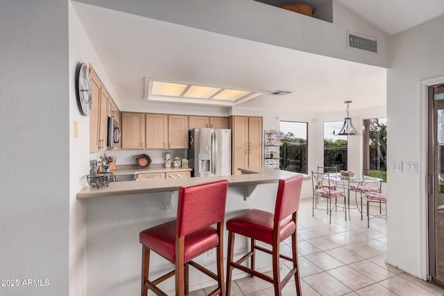 kitchen featuring light brown cabinets, visible vents, light countertops, appliances with stainless steel finishes, and a kitchen bar