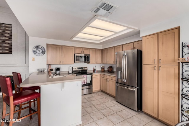 kitchen featuring visible vents, a kitchen bar, appliances with stainless steel finishes, a peninsula, and a sink