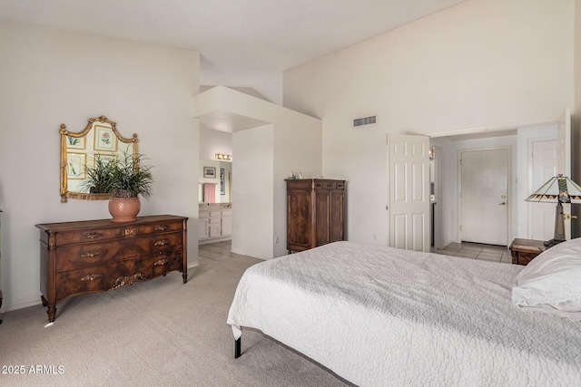 bedroom with visible vents, ensuite bathroom, light colored carpet, and high vaulted ceiling