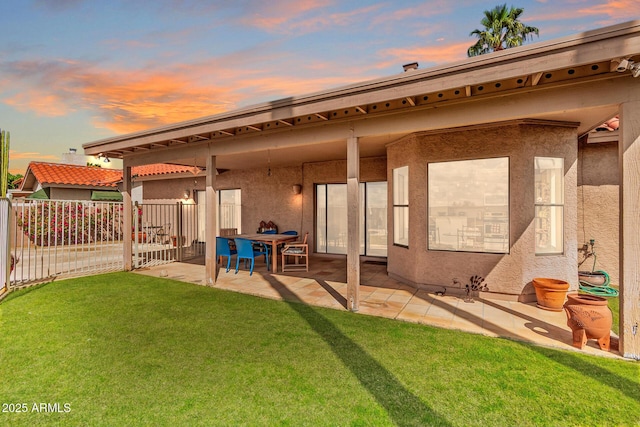 back of property featuring a patio, a lawn, fence, and stucco siding