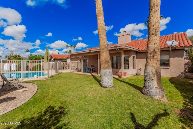 rear view of house with stucco siding, a chimney, a fenced backyard, a yard, and a patio