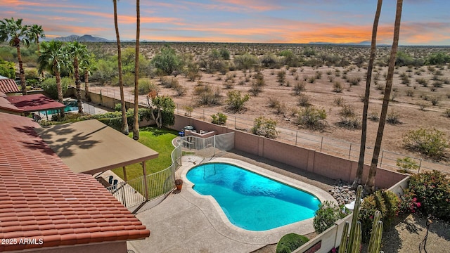 pool at dusk with a patio area, a fenced in pool, a mountain view, and a fenced backyard