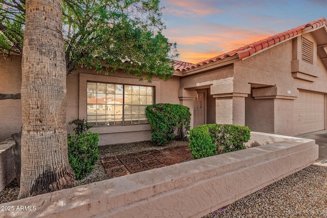 view of front of property featuring stucco siding, a tiled roof, and an attached garage