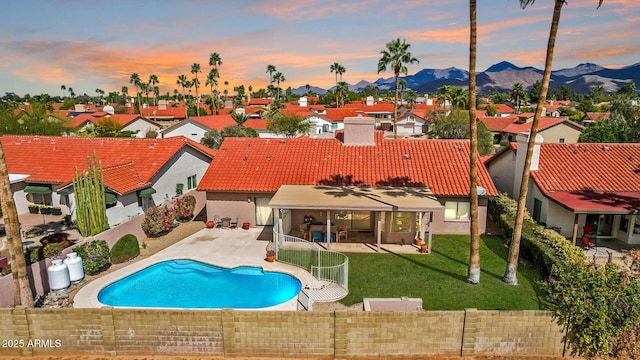 pool at dusk with a residential view, a fenced backyard, a yard, a mountain view, and a patio