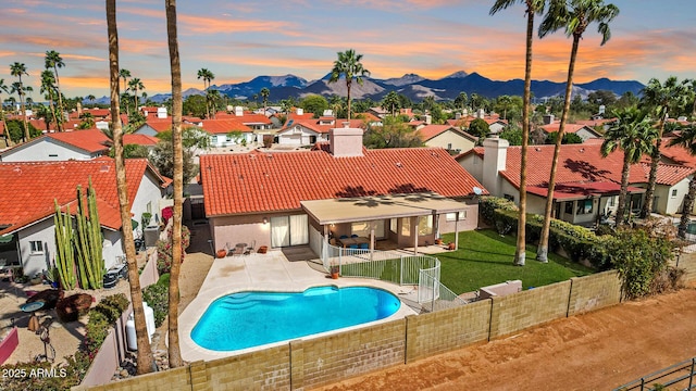 pool at dusk with a residential view, a lawn, a mountain view, and a fenced backyard