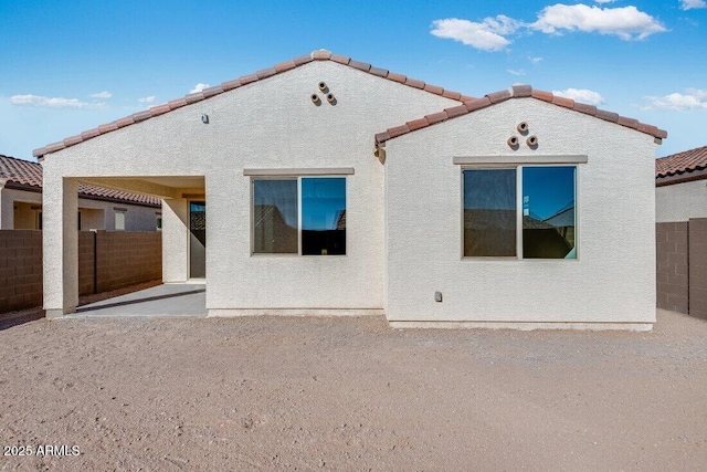 rear view of house with a tiled roof, a patio area, fence, and stucco siding