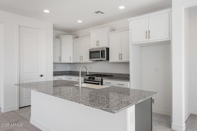 kitchen featuring an island with sink, appliances with stainless steel finishes, light stone counters, white cabinetry, and a sink