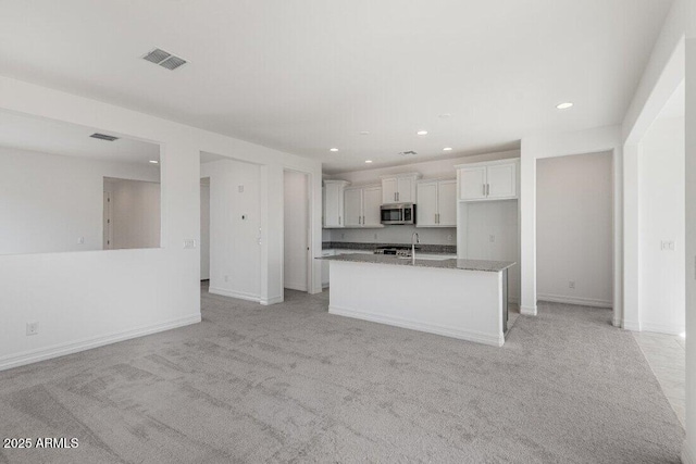 kitchen with open floor plan, stainless steel microwave, a center island with sink, and white cabinetry