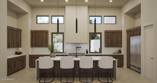 kitchen with stainless steel built in refrigerator, plenty of natural light, a towering ceiling, and a kitchen island with sink