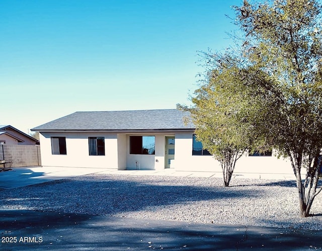 view of front of property featuring a shingled roof, fence, and stucco siding