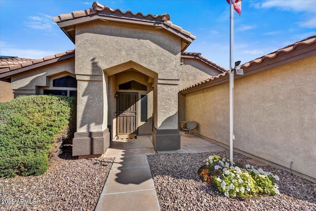 entrance to property with a tiled roof, a patio area, and stucco siding