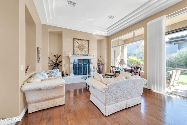 living room with a raised ceiling, a tiled fireplace, and hardwood / wood-style flooring