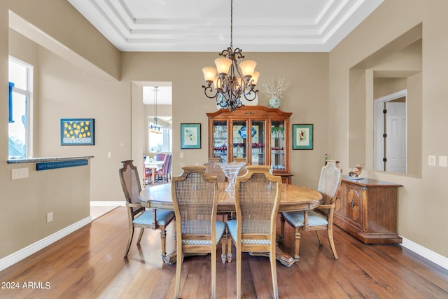 dining room with a wealth of natural light, a raised ceiling, hardwood / wood-style floors, and a notable chandelier