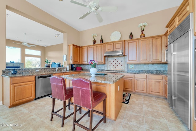 kitchen with kitchen peninsula, a breakfast bar area, appliances with stainless steel finishes, stone counters, and a center island