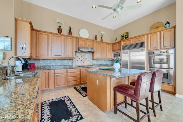 kitchen featuring light stone countertops, sink, built in appliances, and a kitchen island