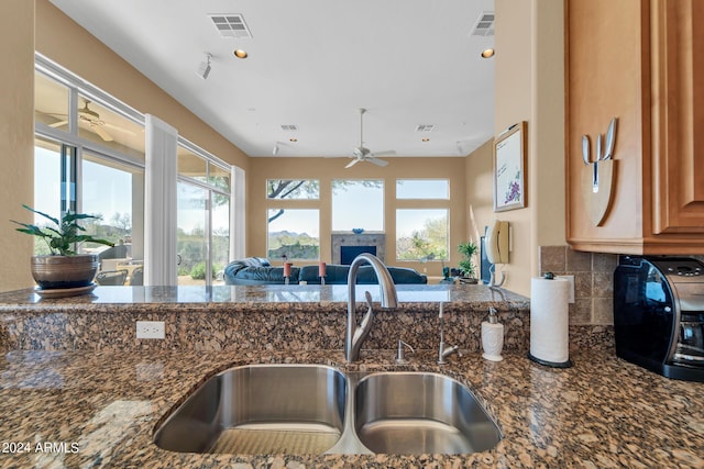 kitchen featuring ceiling fan, sink, backsplash, and dark stone countertops