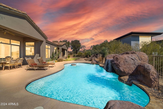 pool at dusk with pool water feature and a patio area