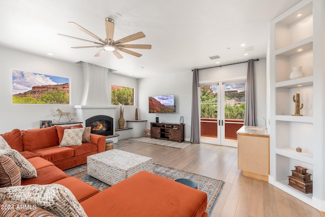 living room with light hardwood / wood-style floors, a large fireplace, ceiling fan, and built in features